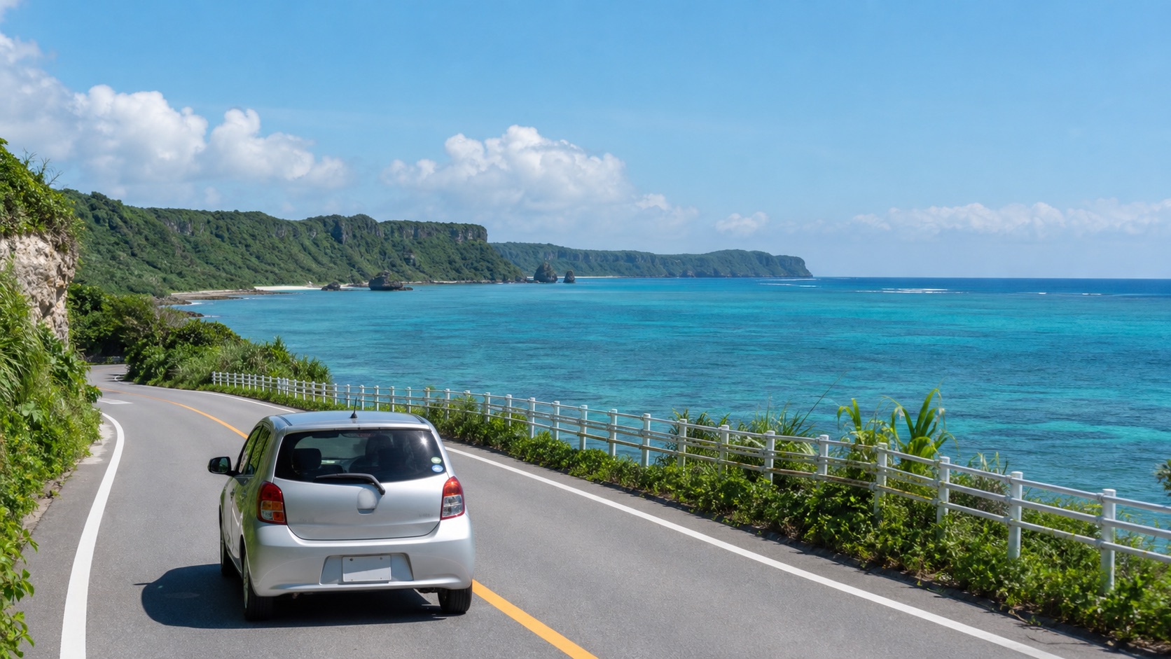 Compact rental car on a coastal road beside Okinawa's turquoise sea